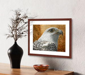 Pastel painting print of a a white gyrfalcon on gold leaf background with a mahogany frame and 2” white mat hanging in an entrance hall.  Rendered in a realistic style by award winning artist Kathie Miller.