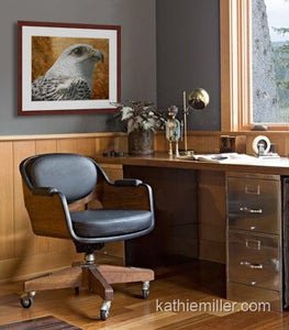 Pastel painting print of a a white gyrfalcon on gold leaf background with a mahogany frame and 2” white mat hanging in a home office.  Rendered in a realistic style by award winning artist Kathie Miller.