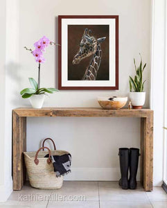 Pastel portrait painting prints of giraffe with a mahogany frame and 2” white mat hanging in an entrance hall. Rendered in a realistic style by award winning artist Kathie Miller.