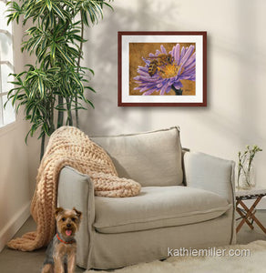 Pastel painting print of a honey bee on a pink flower with gold leaf background with a mahogany frame and 2” white mat hanging in a cozy sitting area.  Rendered in a realistic style by award winning artist Kathie Miller.