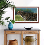 Pastel portrait print of a cheetah in the bright morning sun with a mahogany frame and 2” white mat hanging in a entrance hall.  Rendered in a photo realistic style by award winning artist Kathie Miller.