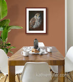 Pastel painting print of an American Kestrel with a mahogany frame and 2” white mat hanging in a dining room.  Rendered in a realistic style by award winning artist Kathie Miller.