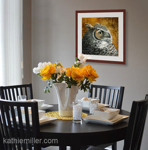 Pastel painting print of a great horned owl with gold leaf background with a mahogany frame and 2” white mat hanging in a casual dining room.  Rendered in a realistic style by award winning artist Kathie Miller.