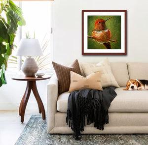 A mock up photo of a elegant living room. Hung on the wall is a print of my painting “A Moment of Rest-Rufus Hummingbird” by award winning artist Kathie Miller. The print has a mahogany frame and white mat. This is a contemporary pastel portrait of a Rufus hummingbird rendered in bold expressive strokes and bright colors. 
