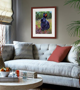 Pastel portrait of a black rabbit sitting among the wildflowers. Print with mahogany frame and a 2” white mat hanging in a cozy sitting room.  Rendered in a contemporary style using bold strokes and bright colors by award winning artist Kathie Miller.