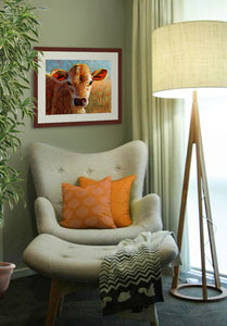 A mock up photo of a quiet sitting area. Hung on the wall is a print of my painting “Brandy-Jersey Calf” by award winning artist Kathie Miller. The print has a mahogany frame and white mat. This is a contemporary pastel portrait of a Jersey calf rendered in bold expressive strokes and bright colors. 