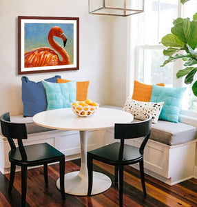 A mock up photo of a dining nook decorated with blues and whites. Hung on the wall is a print of my painting "Cora-Caribbean Flamingo" by award winning artist Kathie Miller. This is a contemporary pastel portrait of a flamingo using bright reds, orange and yellows using expressive strokes. The background is bright blue fading down to a soft blue-green.