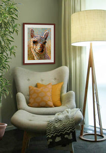 A mock up photo of a quiet sitting area. Hung on the wall is a print of my painting “Eddie-Alpaca” by award winning artist Kathie Miller. The print has a mahogany frame and white mat. This is a contemporary pastel portrait of an alpaca rendered in bold expressive strokes and bright colors. 