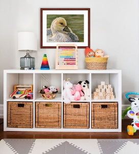 A mock up photo of a child’s play room. Hung on the wall is a print of my painting “Gabby-Gosling” by award winning artist Kathie Miller. The print has a mahogany frame and white mat. This is a contemporary pastel portrait of a young gosling rendered in bold expressive strokes and bright colors. 