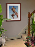 Pastel portrait of a young giraffe and his mother. Print with mahogany frame and a 2” white mat hanging on a stair landing.  Rendered in a contemporary style using bold strokes and bright colors by award winning artist Kathie Miller.