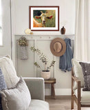 Pastel portrait print of a goat among the flowers framed in mahogany and a white mat  hanging in a country style living room.  Rendered in a contemporary style using bold strokes and bright colors by award winning artist Kathie Miller.