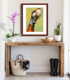 A mock up photo of a rustic entrance hall. Hung on the wall is a print of my painting “Lucy-Goose” by award winning artist Kathie Miller. The print has a mahogany frame and white mat. This is a contemporary pastel portrait of a goose rendered in bold expressive strokes and bright colors. 