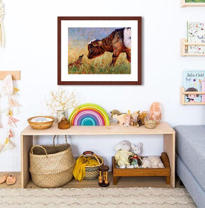 Pastel portrait print of a young goat greeting a tiny field mouse framed in mahogany and a white mat  hanging in a child’s play room.  Rendered in a contemporary style using bold strokes and bright colors by award winning artist Kathie Miller.