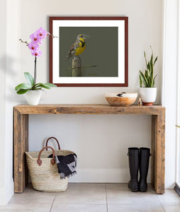 Pastel portrait print of a meadow lark singing in the morning sun with a mahogany frame and 2” white mat hanging in front entrance hall. Rendered in a contemporary style using bold strokes and bright colors by award winning artist Kathie Miller. 