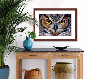 Pastel portrait print of a great horned owl with a mahogany frame and 2” white mat hanging in an entrance hall. Rendered in a contemporary style using bold strokes and bright colors by award winning artist Kathie Miller. 