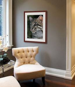 Pastel portrait print of an ocelot with a mahogany frame and 2” white mat hanging in a sitting area of a bedroom. Rendered in a contemporary style using bold strokes and bright colors by award winning artist Kathie Miller. 