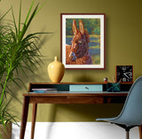 Pastel portrait print of a donkey in the sun with a mahogany frame and 2” white mat hanging in a home office. Rendered in a contemporary style using bold strokes and bright colors by award winning artist Kathie Miller. 