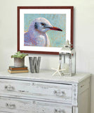A mock up photo of a beach décor entrance hall. Hung on the wall is a print of my painting “Waiting for the Boats to Come In – Sea Gull” by award winning artist Kathie Miller. The print has a mahogany frame and white mat. This is a contemporary pastel portrait of a sea gull rendered in bold expressive strokes and bright colors. 